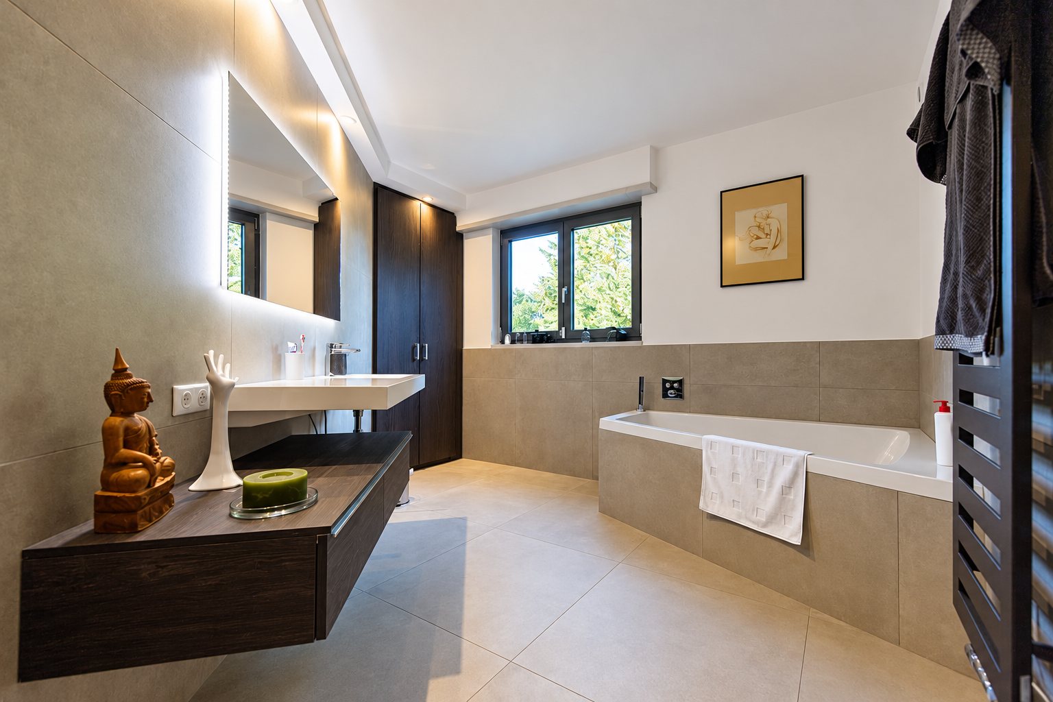 Salle de bains contemporaine rénovée avec baignoire encastrée, vasque suspendue, miroir lumineux, placard sombre et sol en grands carreaux beiges.